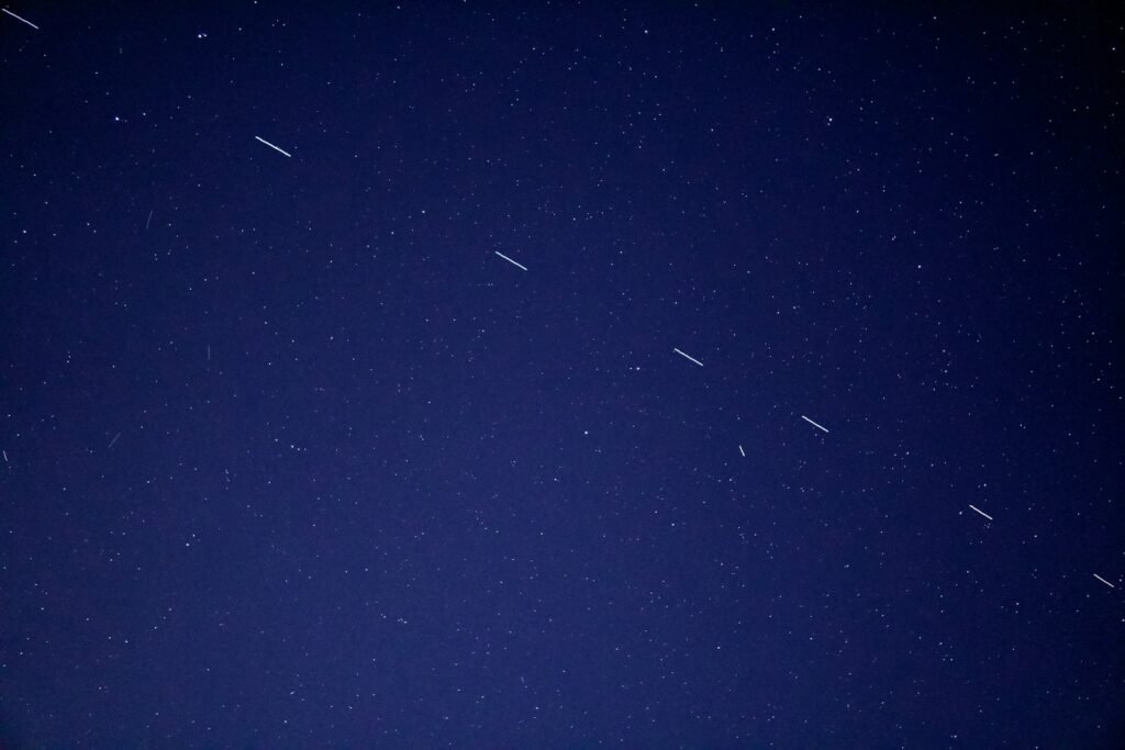 Noční obloha s viditelnými stopami satelitů pohybujících se po obloze.