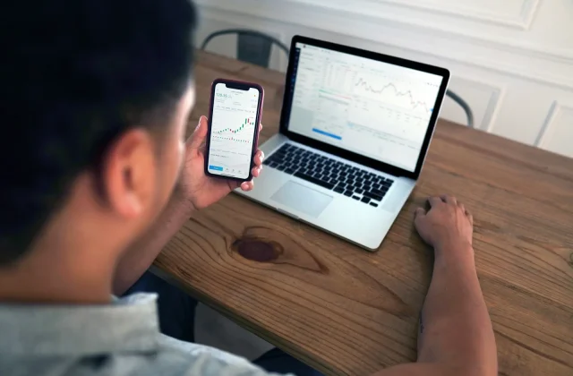 Osoba sleduje grafy na mobilním telefonu, zatímco má na stole notebook. Ideální řešení pro práci i sledování trhu díky stabilnímu připojení, které poskytuje Starlink.