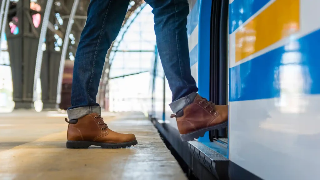 Cestující v kožených botách nastupuje do moderního vlaku na nádraží.