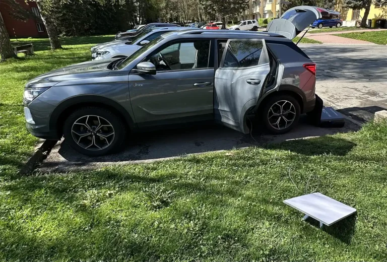 Šedé SUV SsangYong / KGM Korando zaparkované na parkovišti s otevřenými zadními dveřmi a kufrem. Vedle auta na trávě je satelitní anténa Starlink připojená kabelem do vozu.
