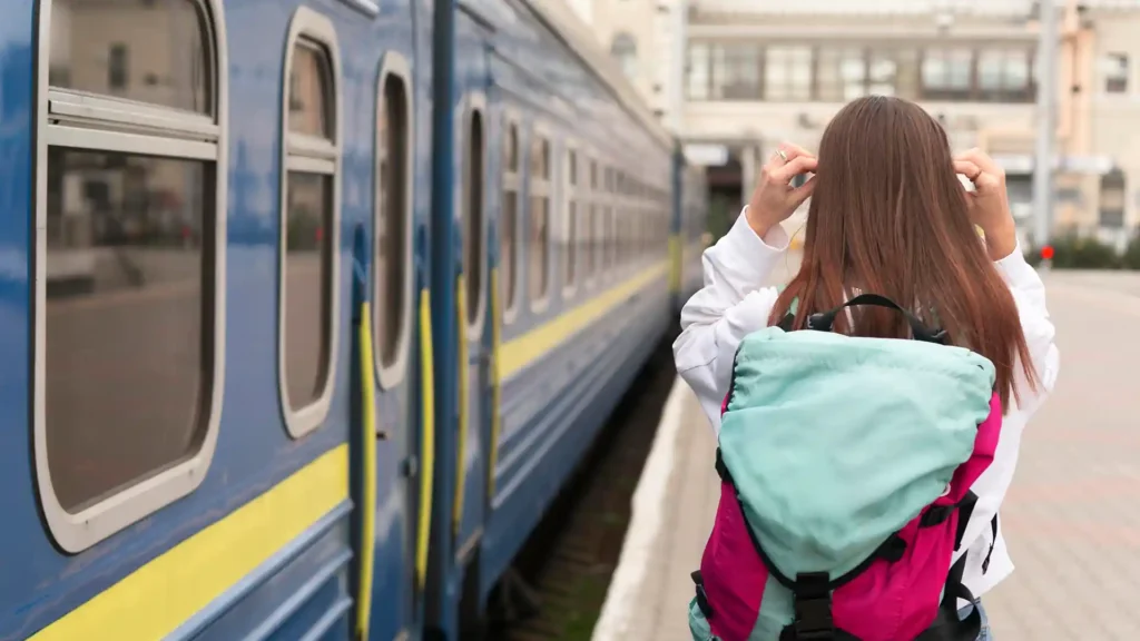 Cestující s batohem čeká na nástupišti u modrého vlaku – moderní cestování vlakem.