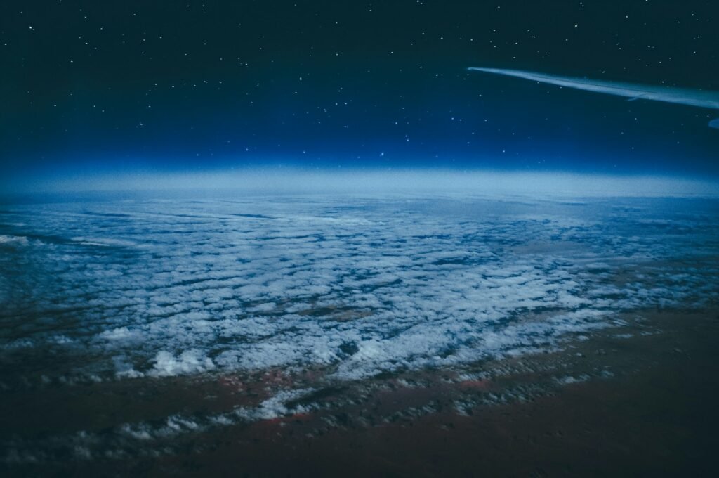 Noční pohled z letadla na hvězdnou oblohu a vrstvy mraků, kde jsou viditelné satelity Starlink na oběžné dráze