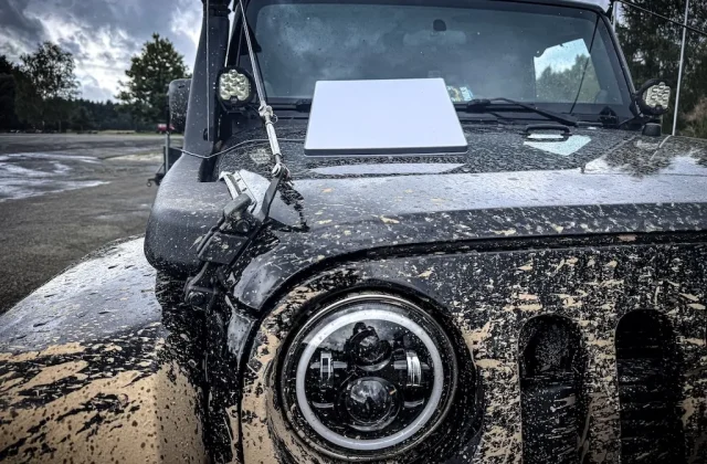 Detailní pohled na předek špinavého Jeepu s notebookem položeným na kapotě po jízdě v terénu.