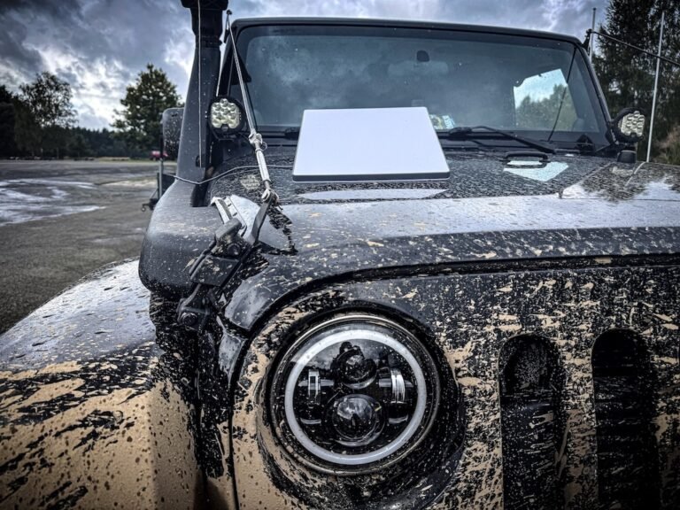 Detailní pohled na předek špinavého Jeepu s notebookem položeným na kapotě po jízdě v terénu.