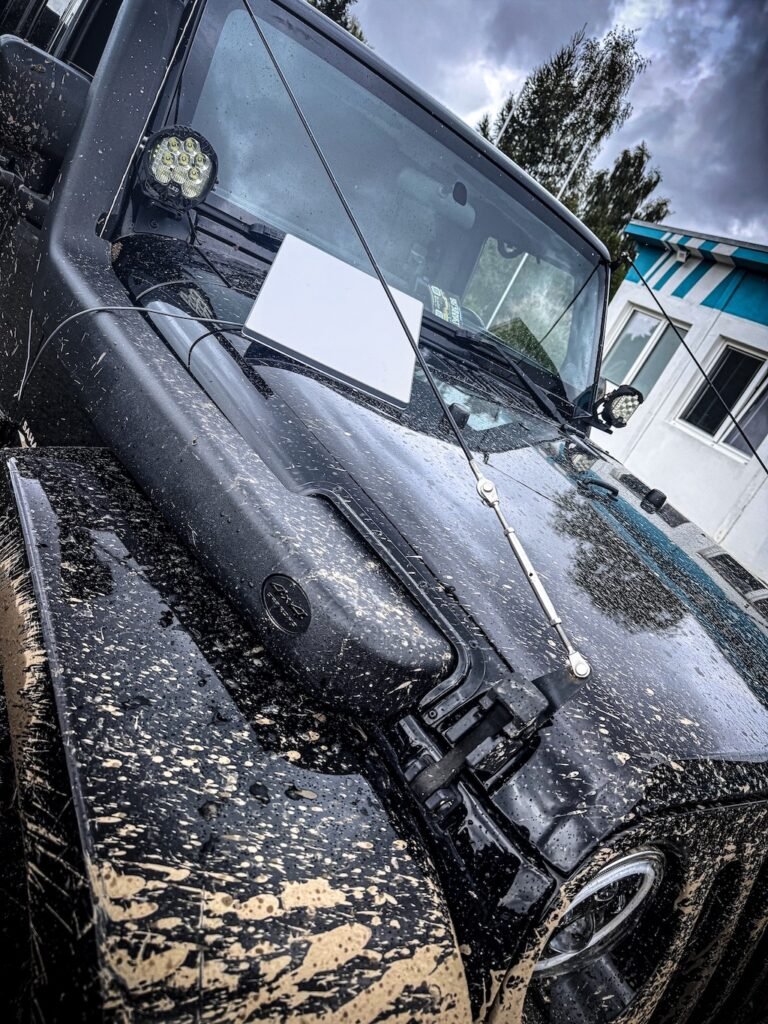 Detail špinavého terénního vozu Jeep po jízdě v blátě s notebookem na kapotě.